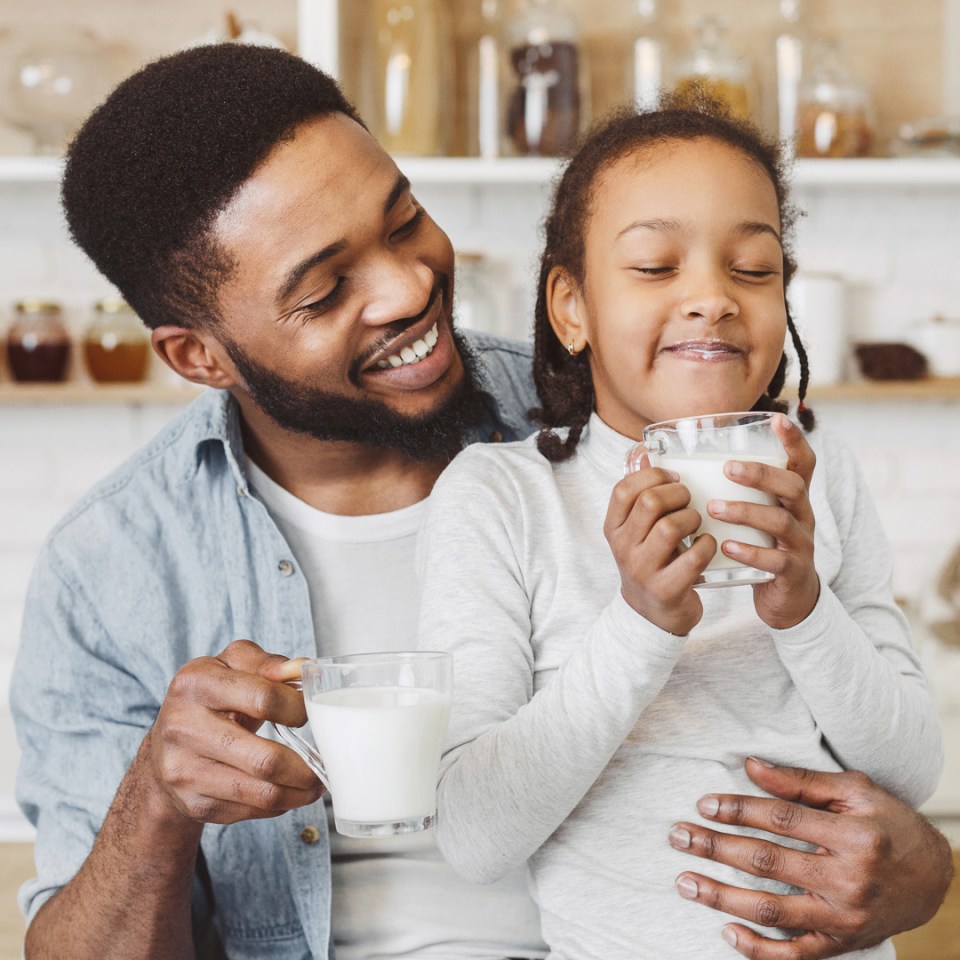 Une fille assise sur les genoux de son père tout en buvant une tasse de lait.