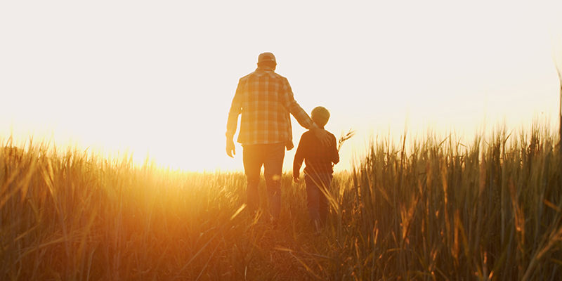 Un homme et un enfant marchant dans un champs vers le soleil