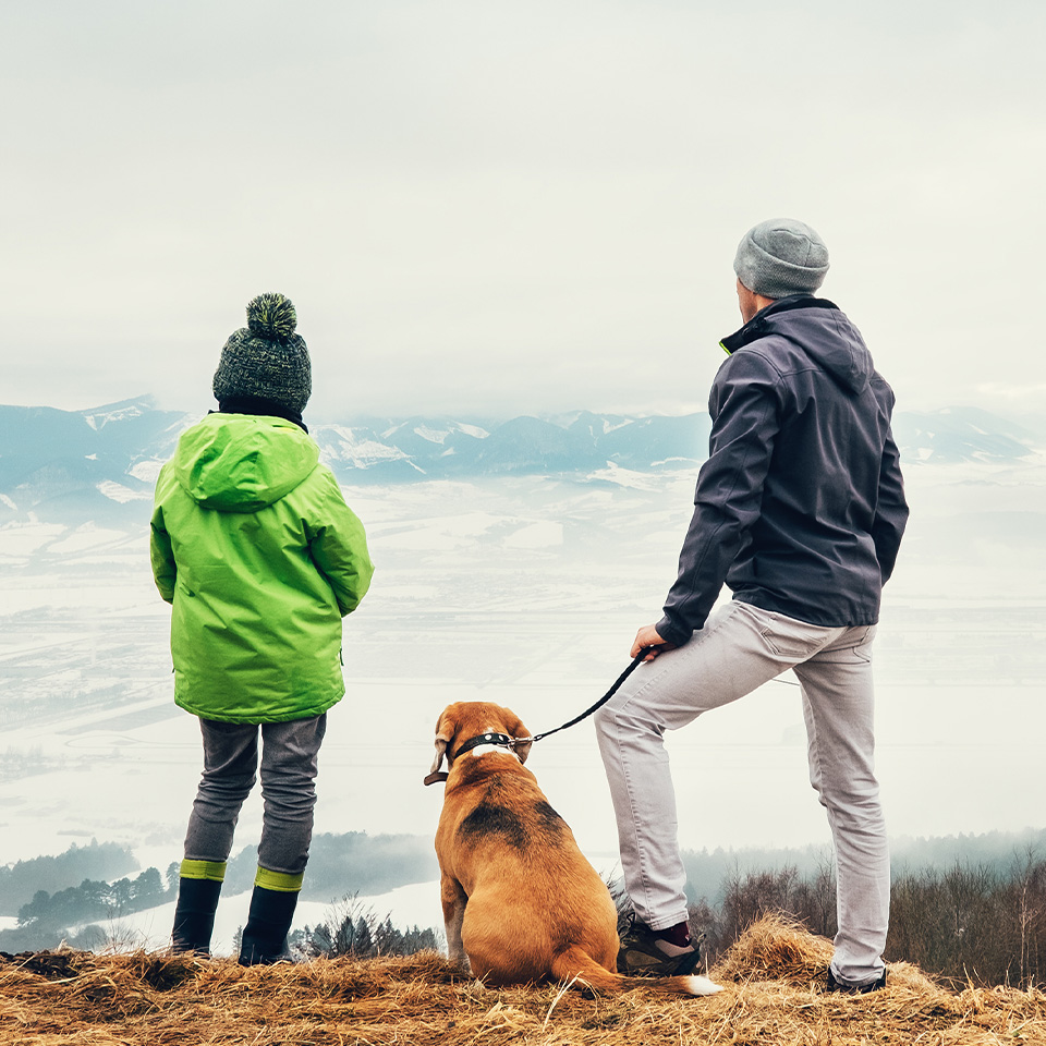 Deux personnes et un chien se tenant sur une colline, profitant de la vue panoramique.