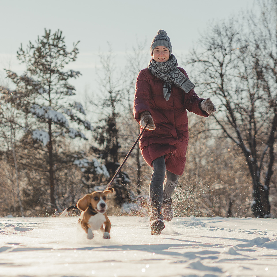 Une femme courant avec son chien dans la neige, tous deux profitant du temps hivernal.